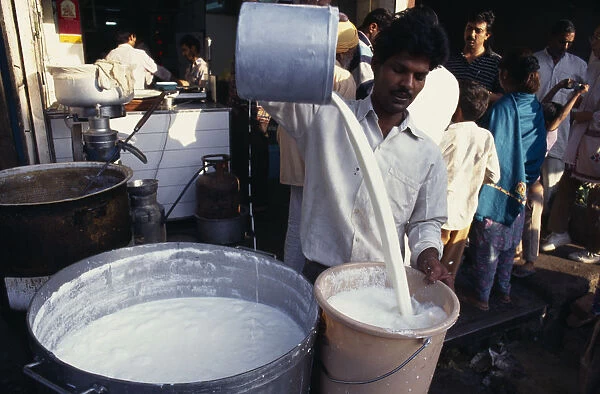 20089379. INDIA Delhi Street market scene with man pouring milk into bucket