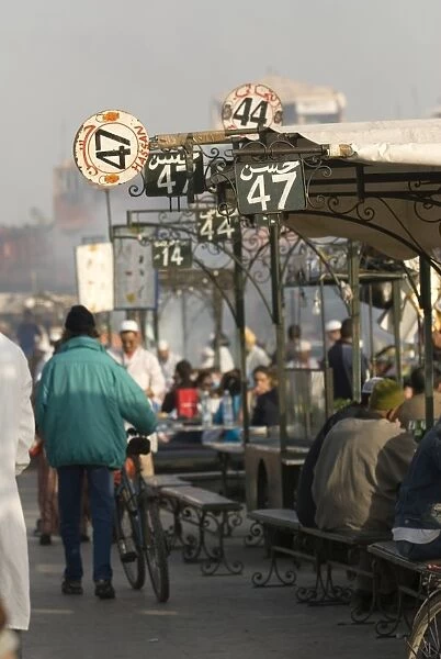 Morocco, Marrakech, Jemaa el Fna, people eating at food stalls, pedestrians walking past