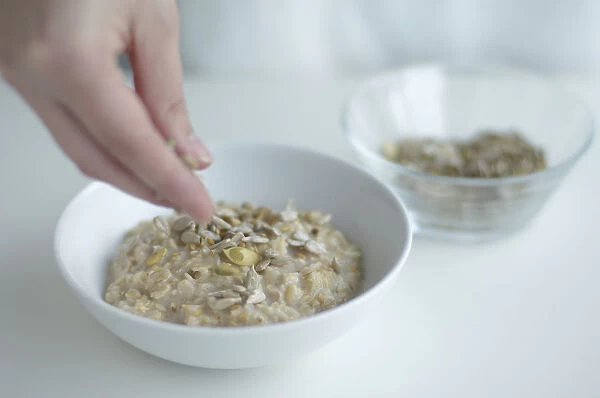 Using fingers to sprinkle sunflower seeds on porridge