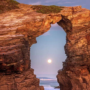Moon thorugh a natural arch at Playa As Catedrais, Bay of Biscay, Costa Verde, Spain