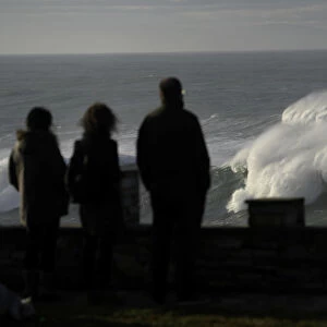 People look at waves as they crash against a lighthouse in the port town of Tapia de