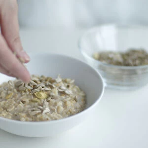 Using fingers to sprinkle sunflower seeds on porridge
