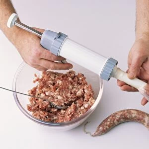 Using sausage stuffer to insert minced garlic and herb salami meat in casing